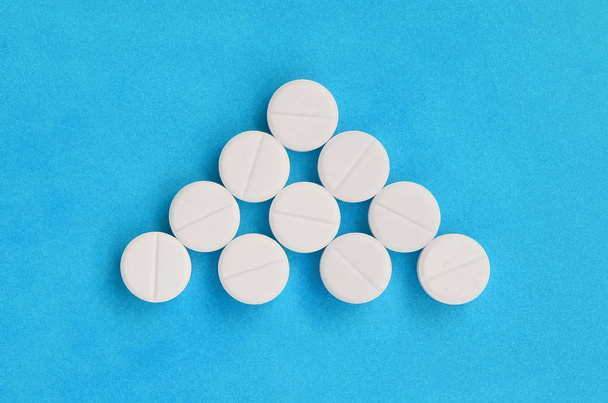 Několik bílých tablet leží na světle modrém pozadí v podobě trojúhelníkovou šipku. Obrázek na pozadí medicíny a farmaceutické témata - Fotografie, Obrázek