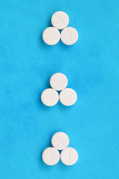 Kilka białych tabletek leżą na jasne niebieskie tło w postaci trzech trójkątnych strzałki. Obraz tła na tematy farmaceutyczny i medycyna - Zdjęcie, obraz