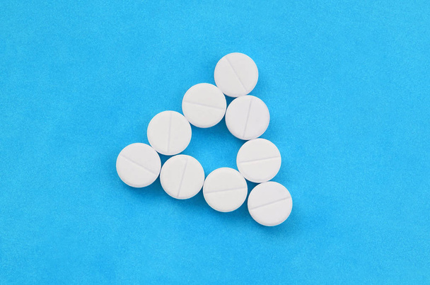 Plusieurs comprimés blancs reposent sur un fond bleu vif sous la forme d'un triangle pair. Image de fond sur la médecine et les sujets pharmaceutiques
 - Photo, image