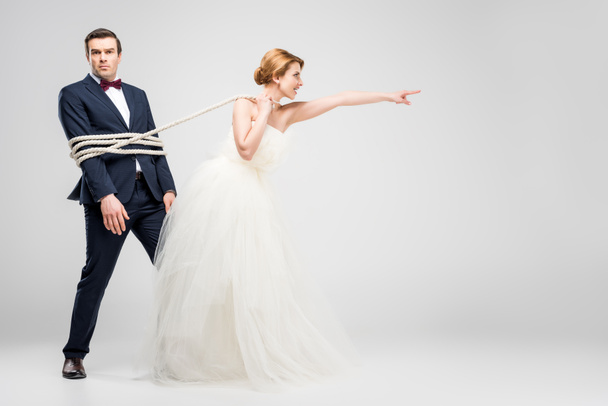 bride pointing and pulling groom bound with rope, isolated on grey, feminism concept - Foto, Bild