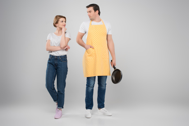 happy wife and husband in apron with frying pan, feminism concept, isolated on grey - Fotó, kép