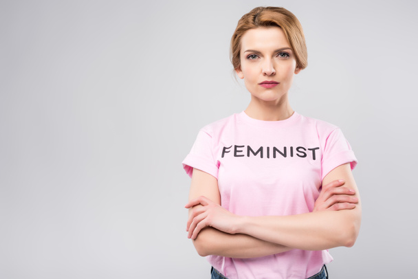 впевнена жінка в рожевій феміністичній футболці з схрещеними руками, ізольована на сірому
 - Фото, зображення