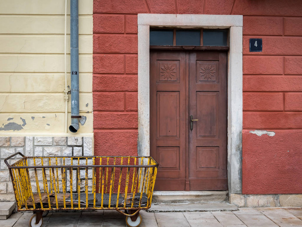 Vieux chariot jaune rouillé devant une vieille porte brune
 - Photo, image