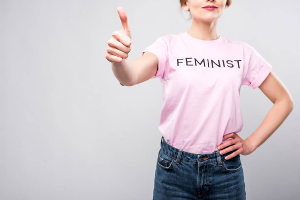 cropped view of woman in pink feminist t-shirt showing thumb up, isolated on grey - Foto, Bild