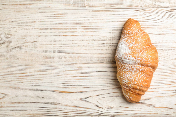 Sabroso croissant con azúcar en polvo sobre fondo de madera, vista superior
 - Foto, Imagen