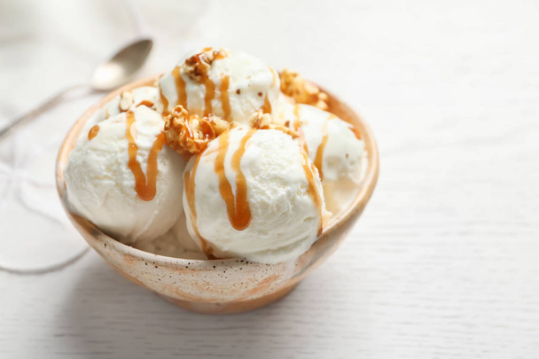 Tasty ice cream with caramel sauce and popcorn in bowl on table - Fotó, kép