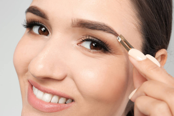 Young woman plucking eyebrow with tweezers, closeup - 写真・画像