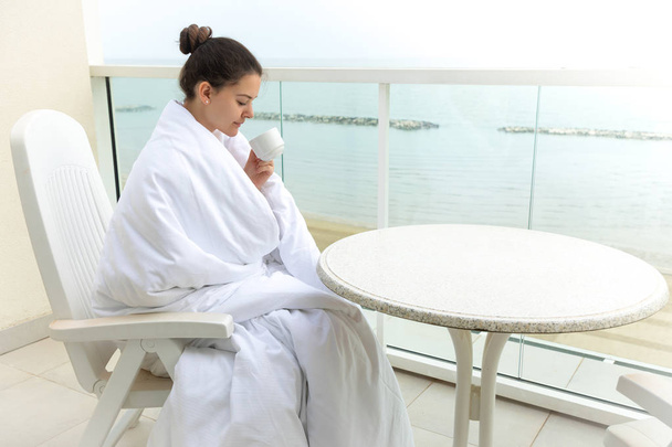 Женщина в белом одеяле пьет кофе на домашней террасе
 - Фото, изображение