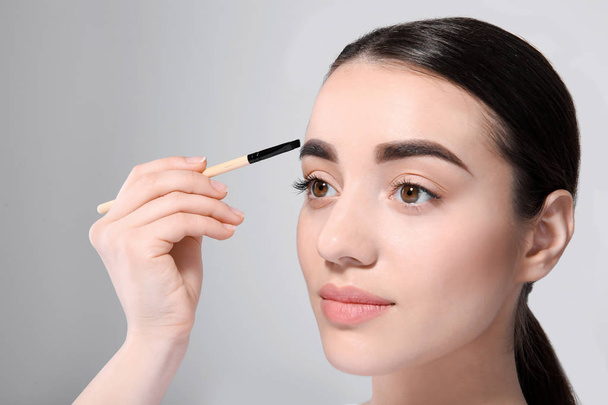 Beautiful woman with perfect eyebrows applying makeup on light background - Zdjęcie, obraz