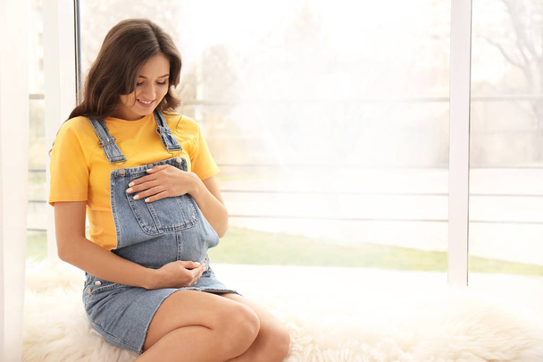 Красивая беременная женщина сидит у окна дома
 - Фото, изображение