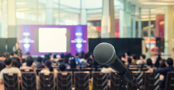 Микрофон над размытой фотографией конференц-зала или зала семинаров со спикерами на сцене и на фоне участников, концепция деловых встреч
 - Фото, изображение