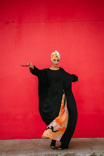 Retrato de moda de una mujer hermosa, alta y de moda de ascendencia de Oriente Medio. Está posando sobre un fondo rojo y liso.
. - Foto, imagen