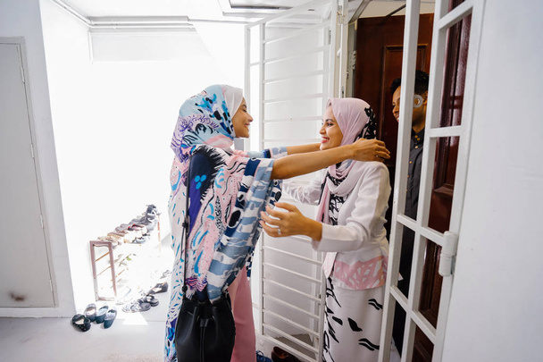 Mulher muçulmana cumprimentando um convidado na porta e convidá-la para celebrar Hari Raya, uma celebração muçulmana de amor e perdão. Estão muito contentes por se verem.
. - Foto, Imagem