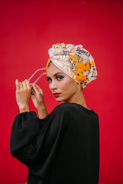 Fashion portrait of a beautiful, tall and fashionable woman of Middle Eastern descent. She is posing against a red, plain background. - 写真・画像