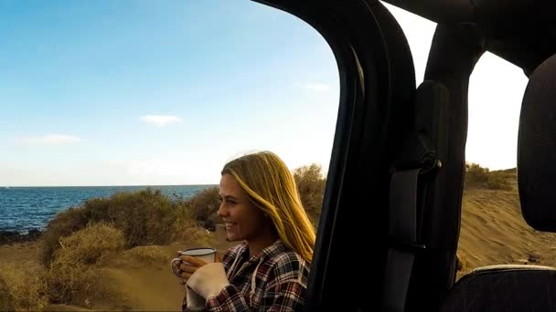 Krásná mladá žena s kávou u auto na pláži - Záběry, video