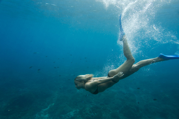 side view of woman in bikini and flippers diving in ocean alone - Foto, afbeelding