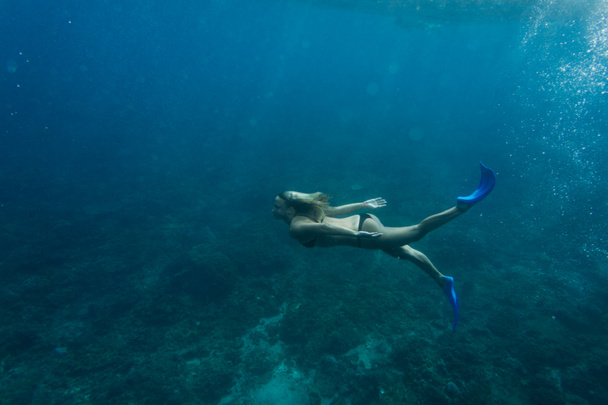 side view of woman in bikini and flippers diving in ocean alone - Фото, зображення