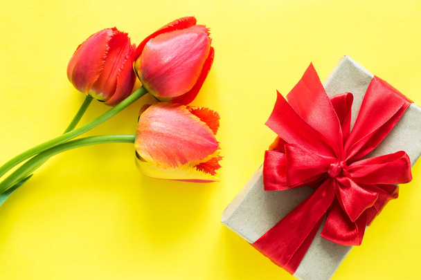 Gift box with red ribbon bow flower Bouquet tulips on bright yellow background - Φωτογραφία, εικόνα