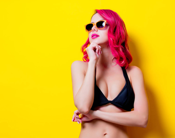 Menina de cabelo rosa nova em biquíni e óculos de laranja. Retrato isolado sobre fundo amarelo
 - Foto, Imagem
