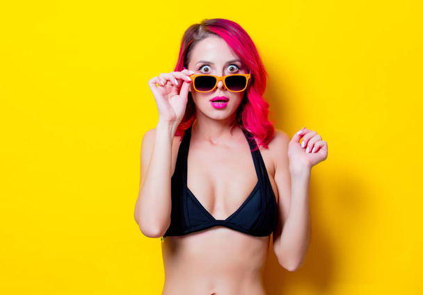 Fiatal rózsaszín haj lány a bikini és a narancsszínű szemüveg. Portré, elszigetelt, a sárga háttér - Fotó, kép