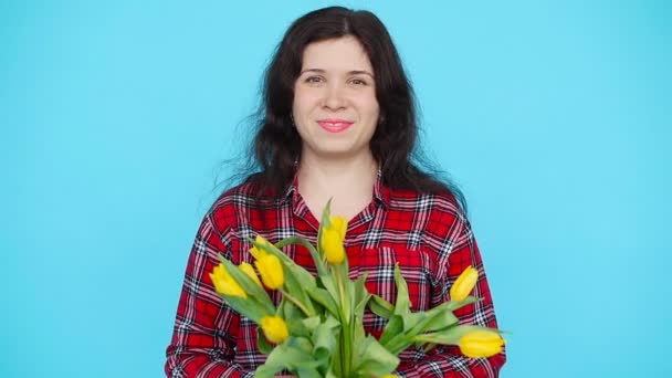 Młoda kobieta z kwiatów tulipany w ręce na niebieskim tle - Materiał filmowy, wideo