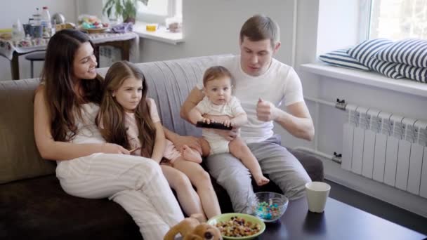 portret przyjazny rodzinie, człowiek, jego żona i ich dzieci, oglądając telewizję, siedząc w salonie pokoju na kanapie - Materiał filmowy, wideo