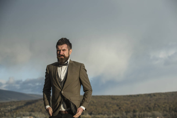 Bearded man on cloudy sky. Hipster with beard and mustache on unshaven face. Fashion businessman wear classic coat with bow tie. Freedom and success. Vacation travelling and wanderlust, copy space - Fotografie, Obrázek