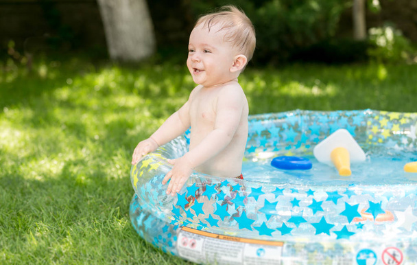 Happy laughing baby boy jumping in inflatable swimming pool in backyard - Foto, Imagem