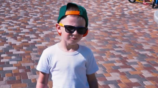 Młody chłopak w okulary przeciwsłoneczne i czapka, idąc ulicą, dziecko 6-letniego spaceru, zwolnionym tempie - Materiał filmowy, wideo