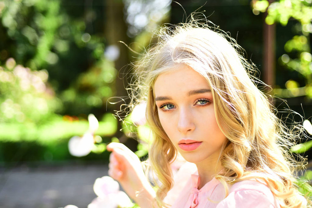 Girl on dreamy face, tender blonde looks at camera, nature background, defocused. Lady walks in park on sunny spring day. Sunny day concept. Young woman enjoy nature in garden. - Fotografie, Obrázek