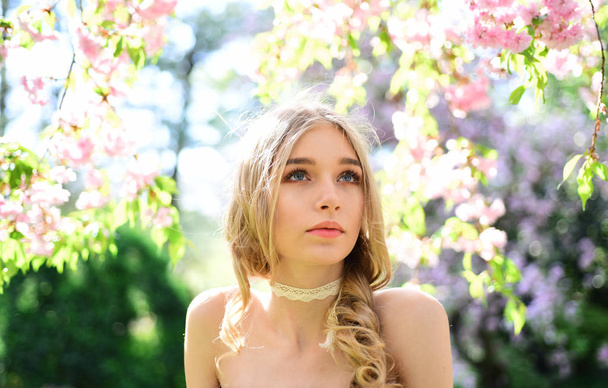 Girl on dreamy face, tender blonde looks at camera, nature background, defocused. Tenderness concept. Young woman enjoy nature in garden. Lady walks in park on sunny spring day. - Photo, Image