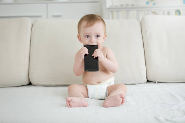 Imádnivaló baba fiú ül a kanapén, és csípős smartphone portréja - Fotó, kép