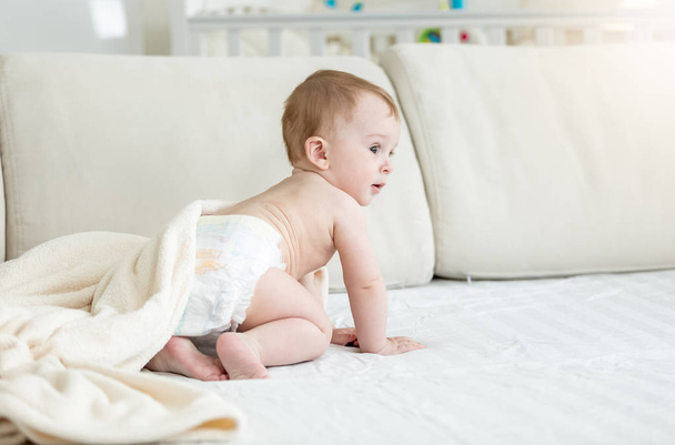Adorable 10 months old baby boy in diapers sitting on sofa - Foto, Imagem
