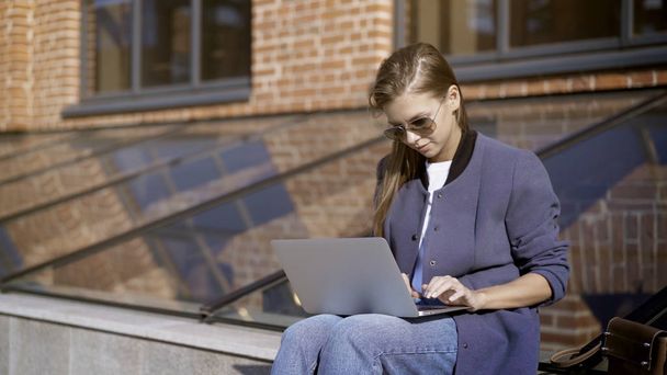 A young pretty girl in sunglasses is working with a laptop outisde - Foto, afbeelding
