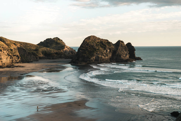 Rock formacje na wybrzeżu Nowej Zelandii Piha plaża, złoto światło w zachód słońca, fale plaży. - Zdjęcie, obraz