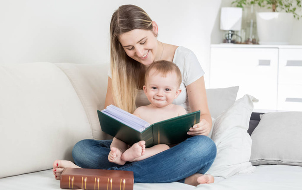 Gelukkig lachende babyjongen lezen van grote oude boek op bed met moeder - Foto, afbeelding