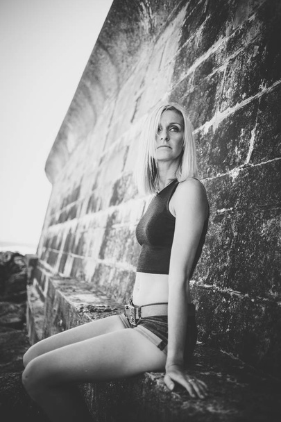 Portrait of blond sporty female model in denim shorts on brick wall background  - Фото, зображення