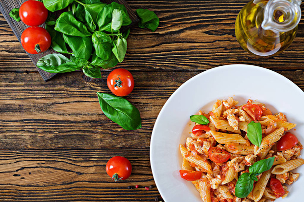 Вид сверху на Penne pasta в томатном соусе с курицей, помидорами, украшенном пелем на деревянном столе. Итальянская еда. Паста-Болоньезе
.  - Фото, изображение