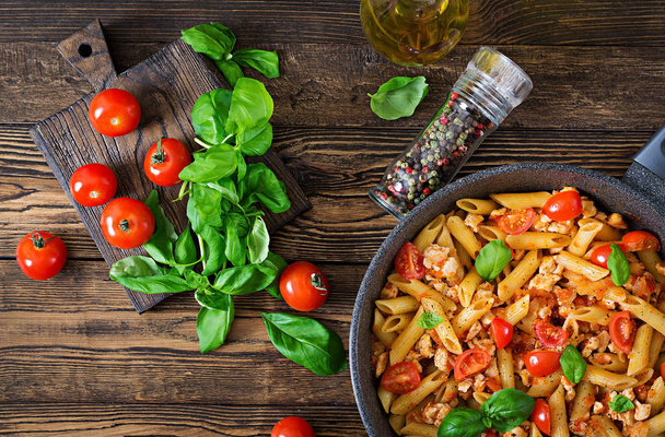 トップ ビュー チキン入りトマトソースのパスタはペンネのトマト、バジルの木製テーブルで飾られました。イタリア料理。パスタ ボロネーゼ。平面図です。フラットを置く - 写真・画像