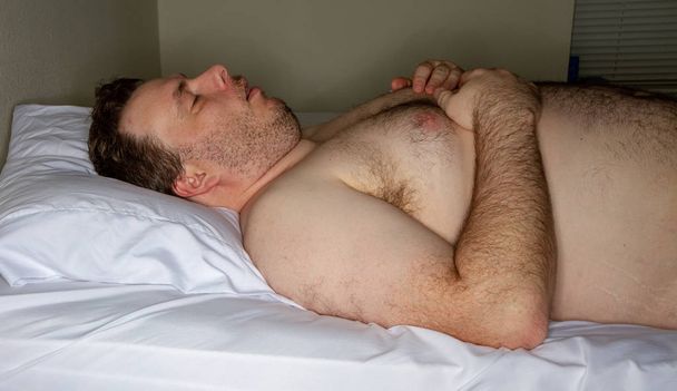 lihava yläosaton mies nukkuu sängyssä
 - Valokuva, kuva