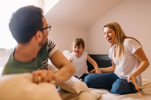 Cute happy child with parents having pillow fight in bed at home - Fotó, kép