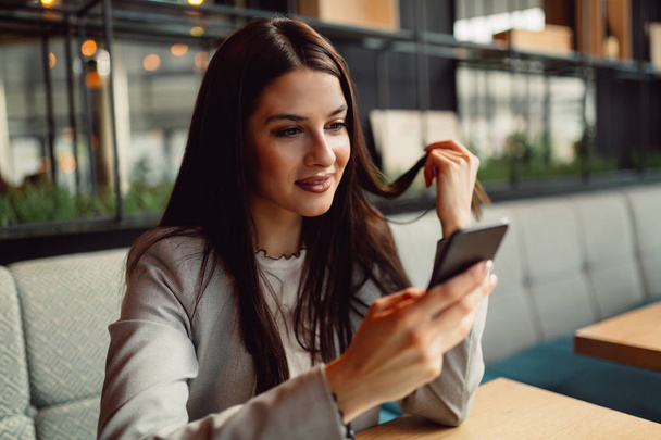 Happy brunette käsittelyssä hyviä uutisia hänen älypuhelin istuessaan kahvilassa
 - Valokuva, kuva