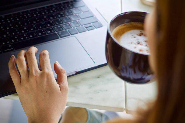 Женщина с помощью ноутбука работает и пить кофе чашку горячей
 - Фото, изображение