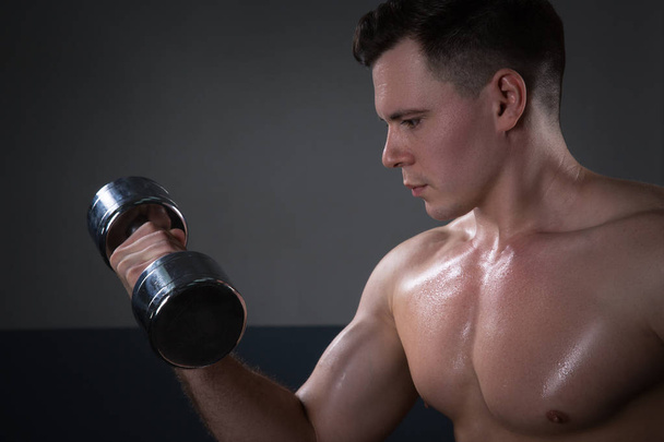 Pohledný mladý muž v šortkách, dělat cvičení pro biceps, na tmavém pozadí v ateliéru - Fotografie, Obrázek