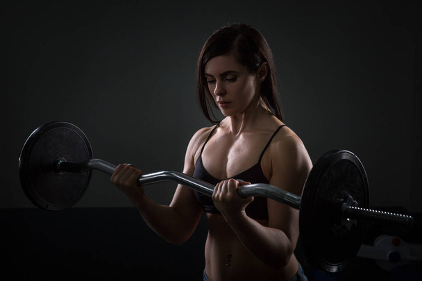 Portrait of athlete girl lifting dumbbells on dark background - Photo, image