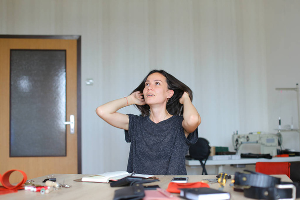 Kaukázusi nő ül a bőr atelier, és így kézzel készített notebook, smartphone, tábla. - Fotó, kép