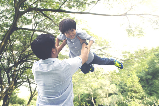 Portrait of happy little boy being lifted by his father while playing together in the park - Valokuva, kuva