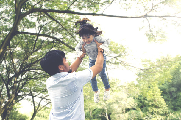 Picture of Asian man lifting his daughter while spending time together in the park - Foto, afbeelding