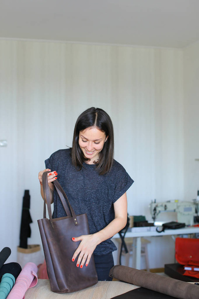 Gelukkige vrouw bruin lederen handgemaakte tas bij atelier maken. - Foto, afbeelding
