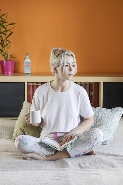 Blonde-haired pretty lady in pajamas is drinking her morning cof - Foto, imagen